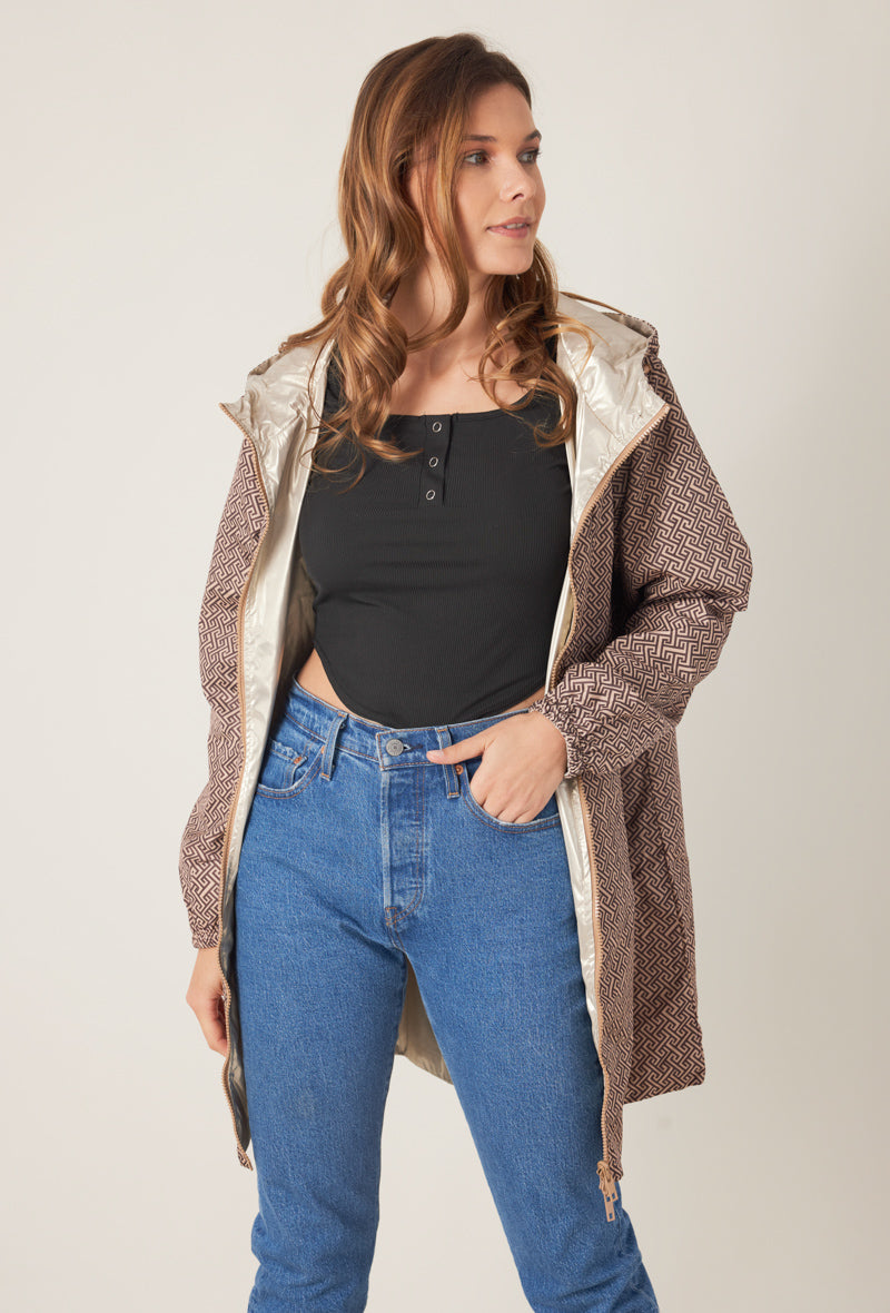 Femme portant la parka réversible LINA taupe à motif géométrique, capuche dorée visible, vue de face
#couleur_taupe