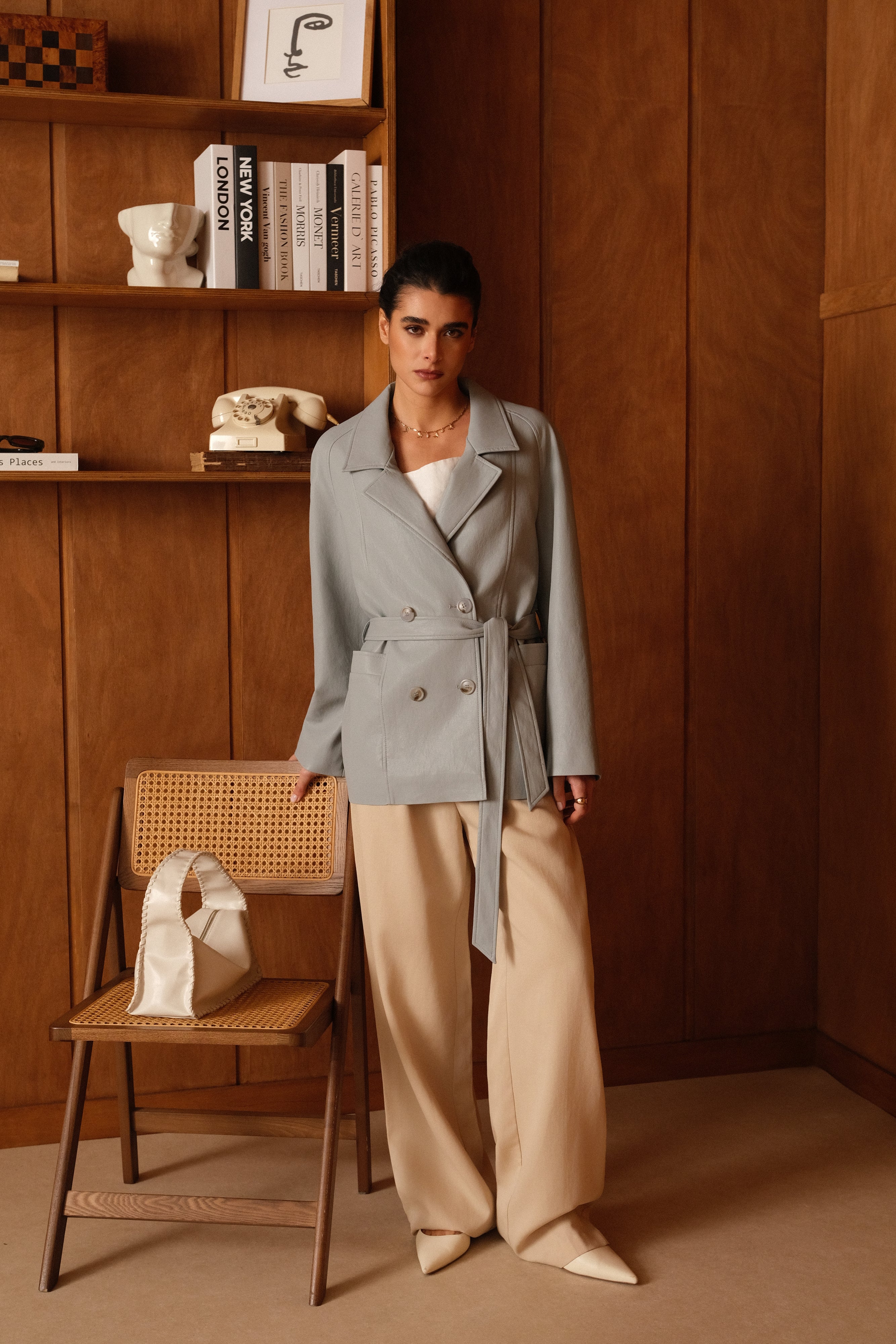 Femme portant veste ovania bleu ciel en similicuir, veste de tailleur col à revers, découpes verticales, fermeture à boutons, ceinture et passants
#couleur_ciel