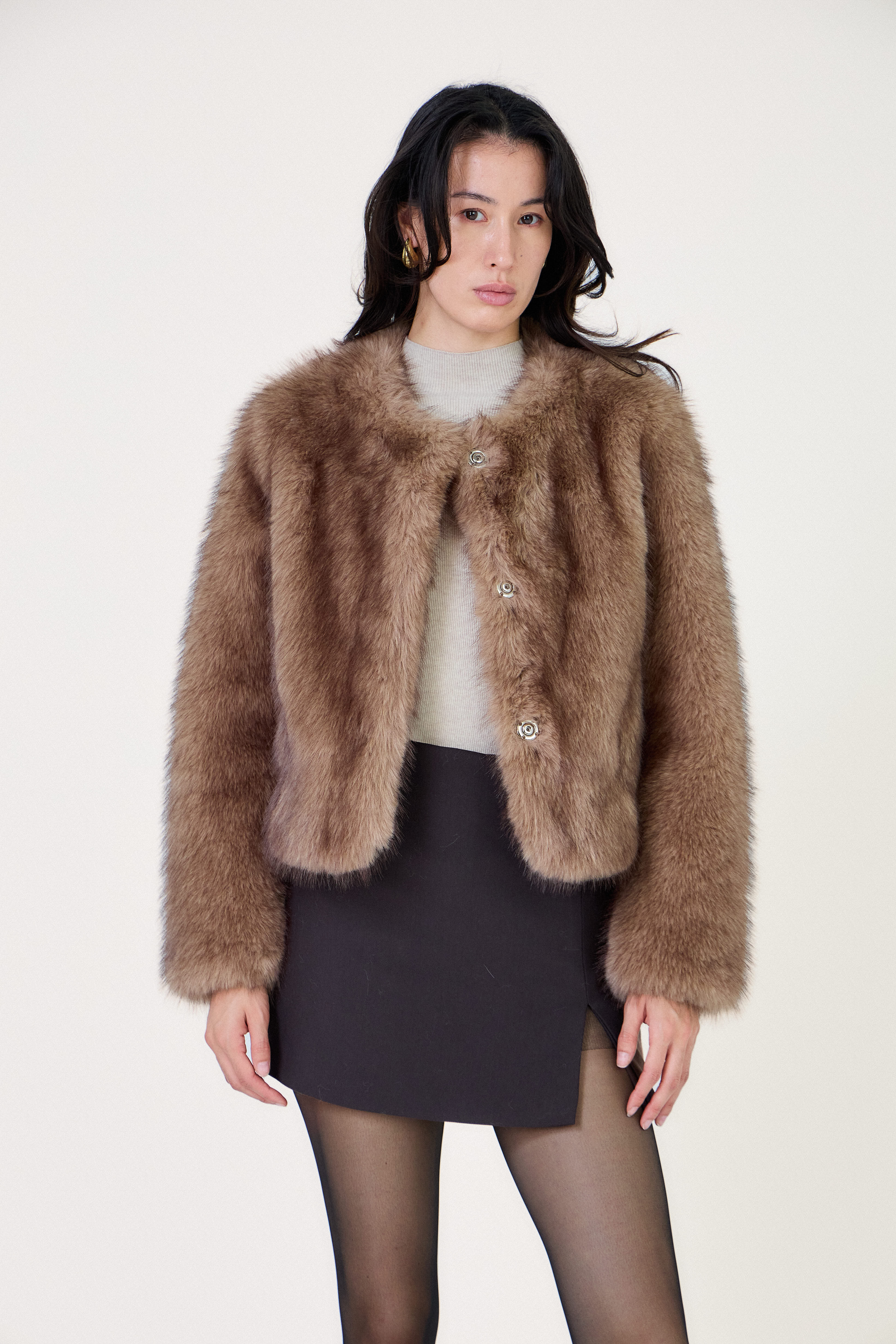 Manteau court en fausse fourrure femme Escandelle Paris, coloris brun, col rond, fermeture à pressions dissimulées, coupe élégante et poils longs doux.
#couleur_taupe