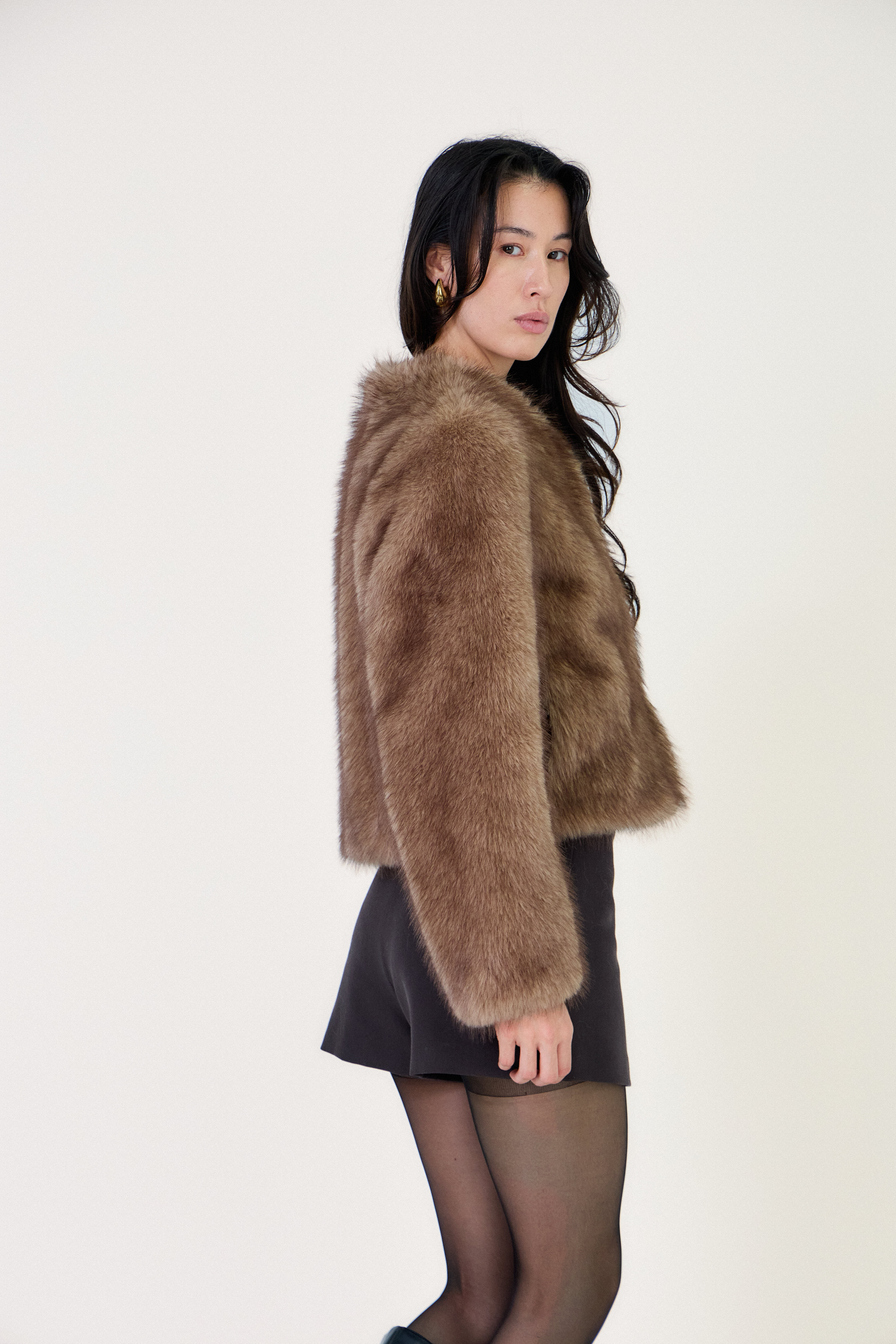 Manteau court en fausse fourrure femme Escandelle Paris, coloris brun, col rond, fermeture à pressions dissimulées, coupe élégante et poils longs doux.
#couleur_taupe