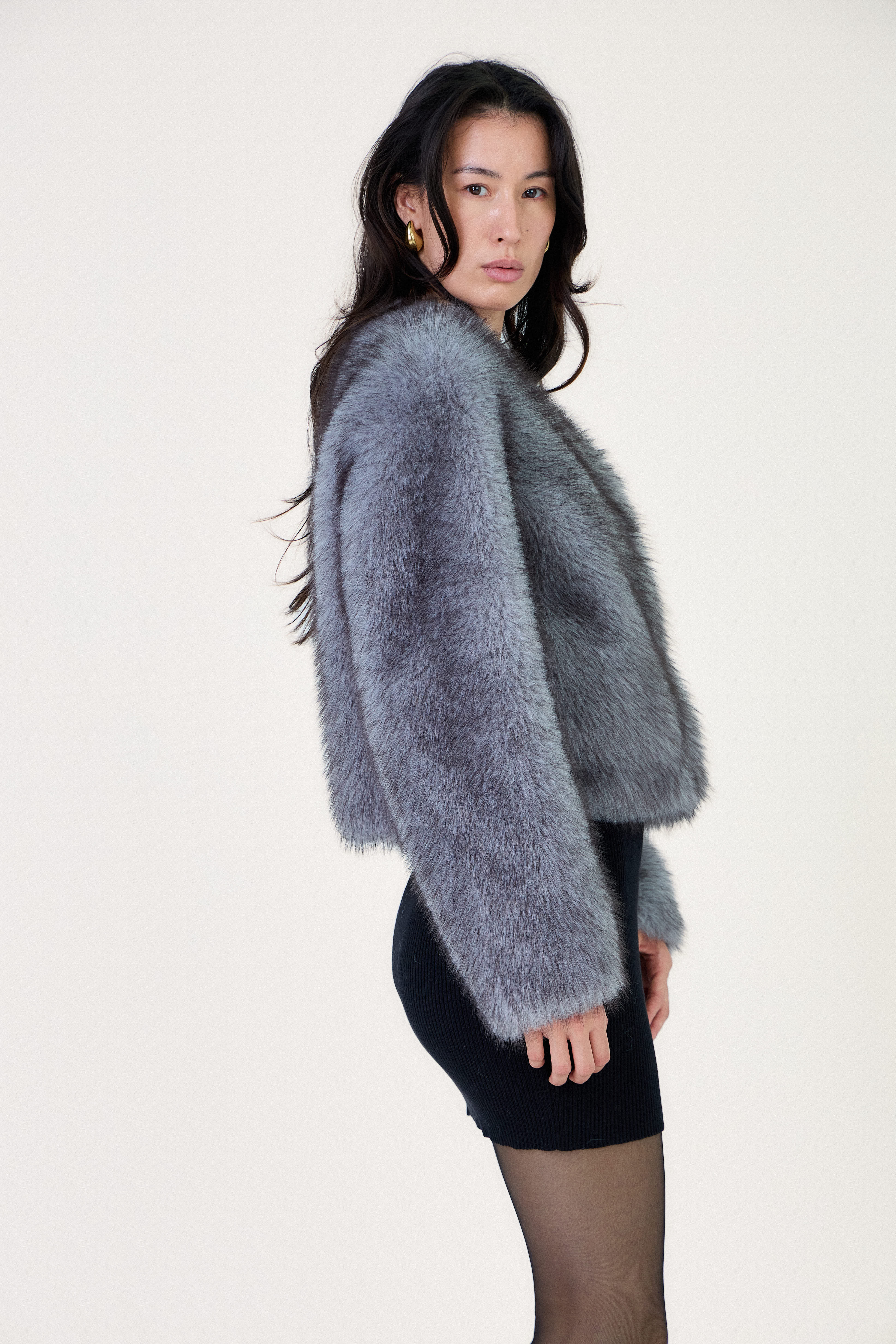 Manteau court en fausse fourrure femme Escandelle Paris, coloris gris, col rond, fermeture à pressions dissimulées, coupe élégante et poils longs doux.
#couleur_gris