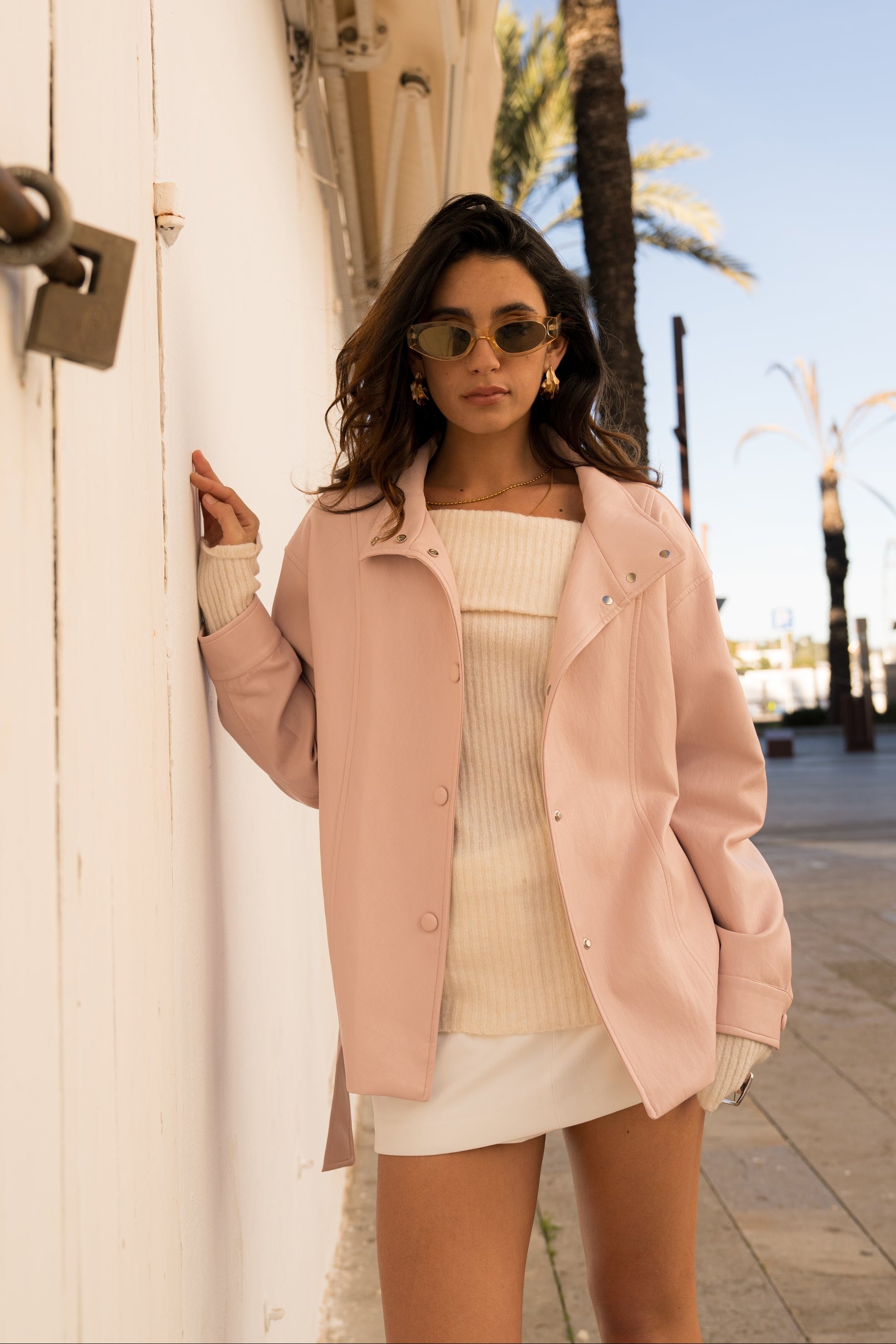 femme portant une veste en similicuir ouverte et fermeture à boutons pressions. Manches longues et boutons poignets. Découpe verticales devant, col montant, devant
#couleur_rose