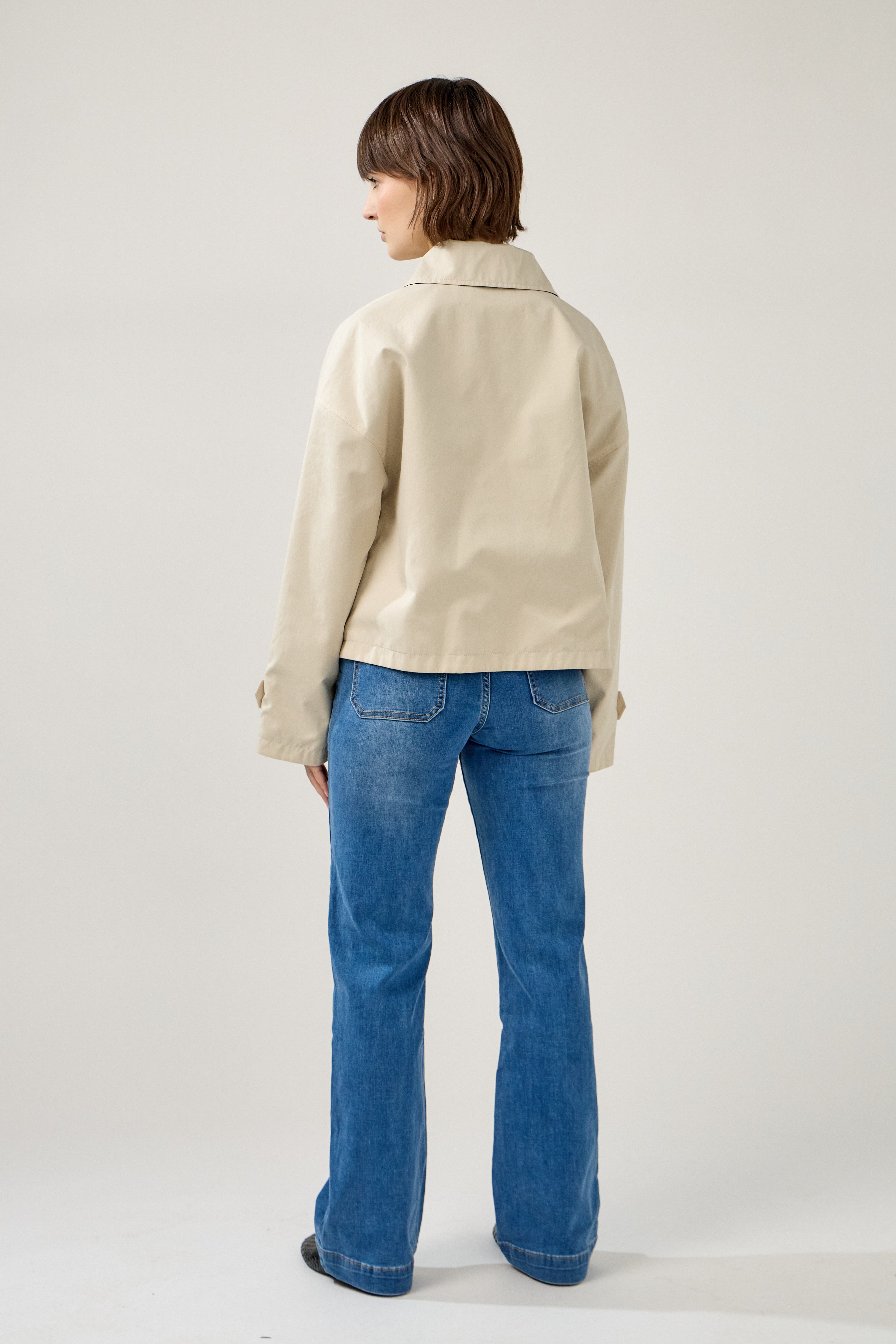 femme portant un veste style trench réversible imperméable, fermeture à boutons, poches et col français, dos
#couleur_beige