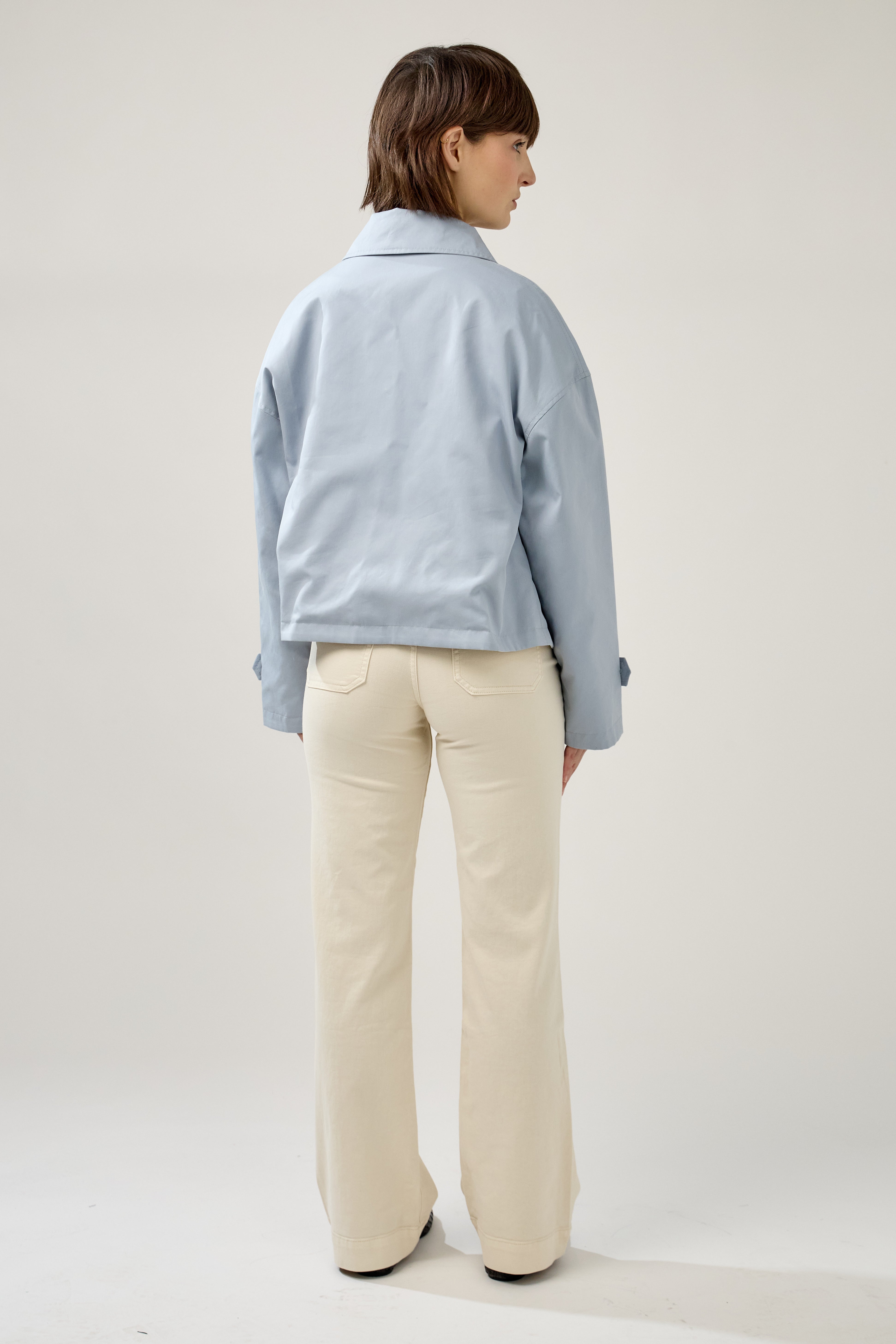 femme portant un veste style trench réversible imperméable, fermeture à boutons, poches et col français, dos
#couleur_ciel