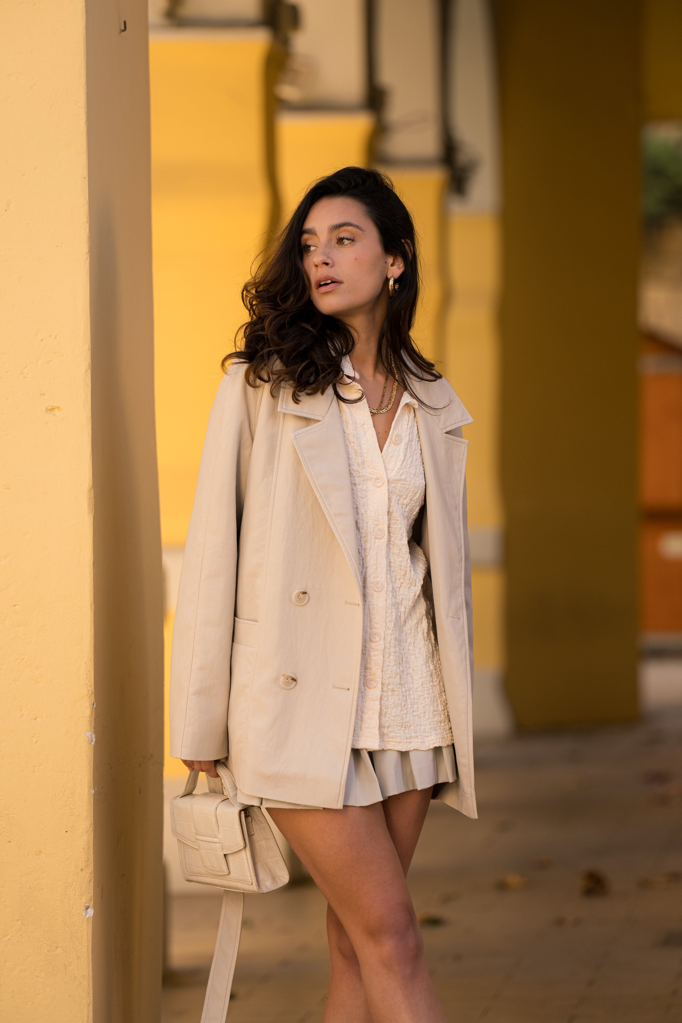 Femme portant veste ovania beige clair en similicuir, veste de tailleur col à revers, découpes verticales, fermeture à boutons, ceinture et passants, devant
#couleur_beige
