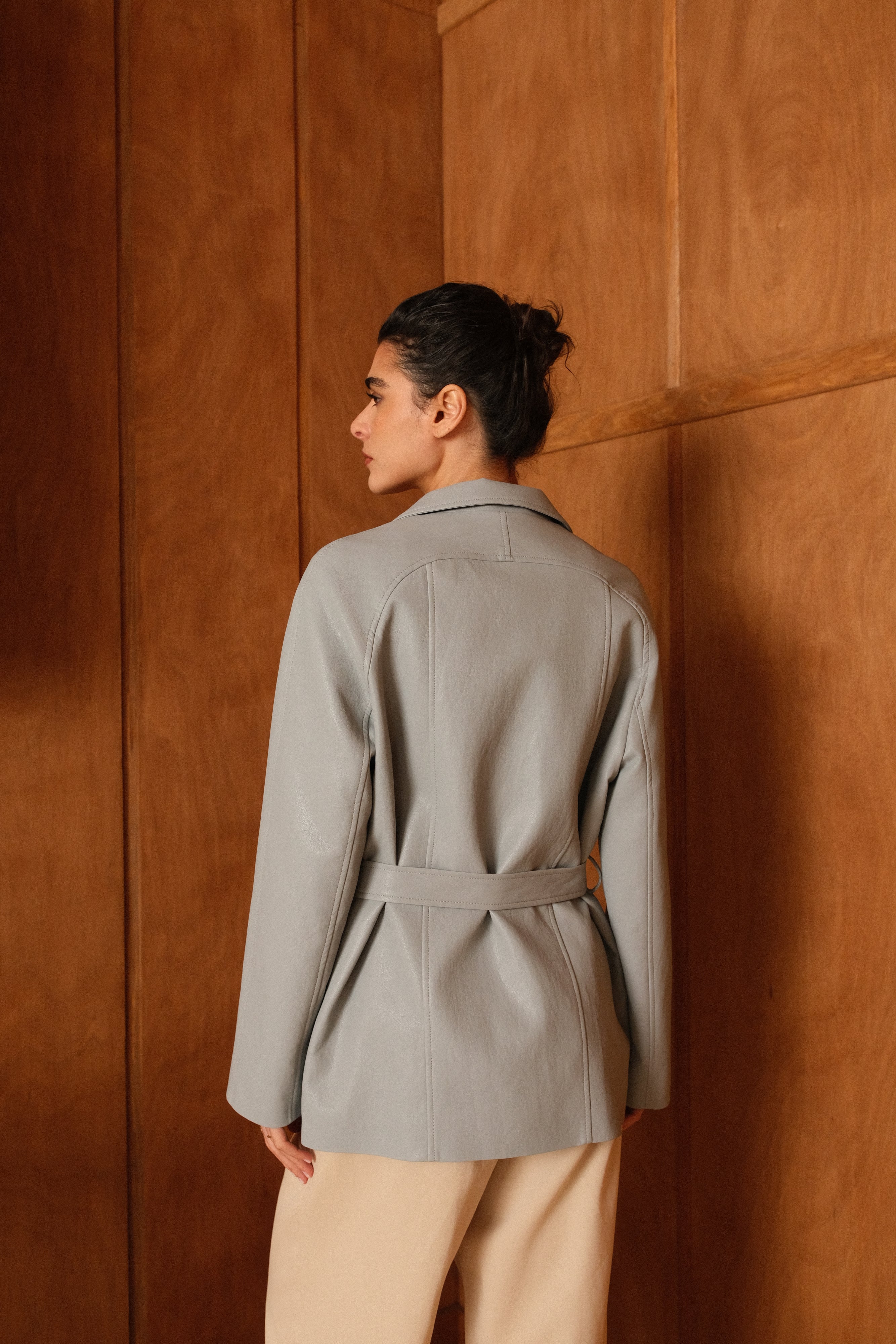 Femme portant veste ovania bleu ciel en similicuir, veste de tailleur col à revers, découpes verticales et arrondi dos ceinture et passants, dos
#couleur_ciel