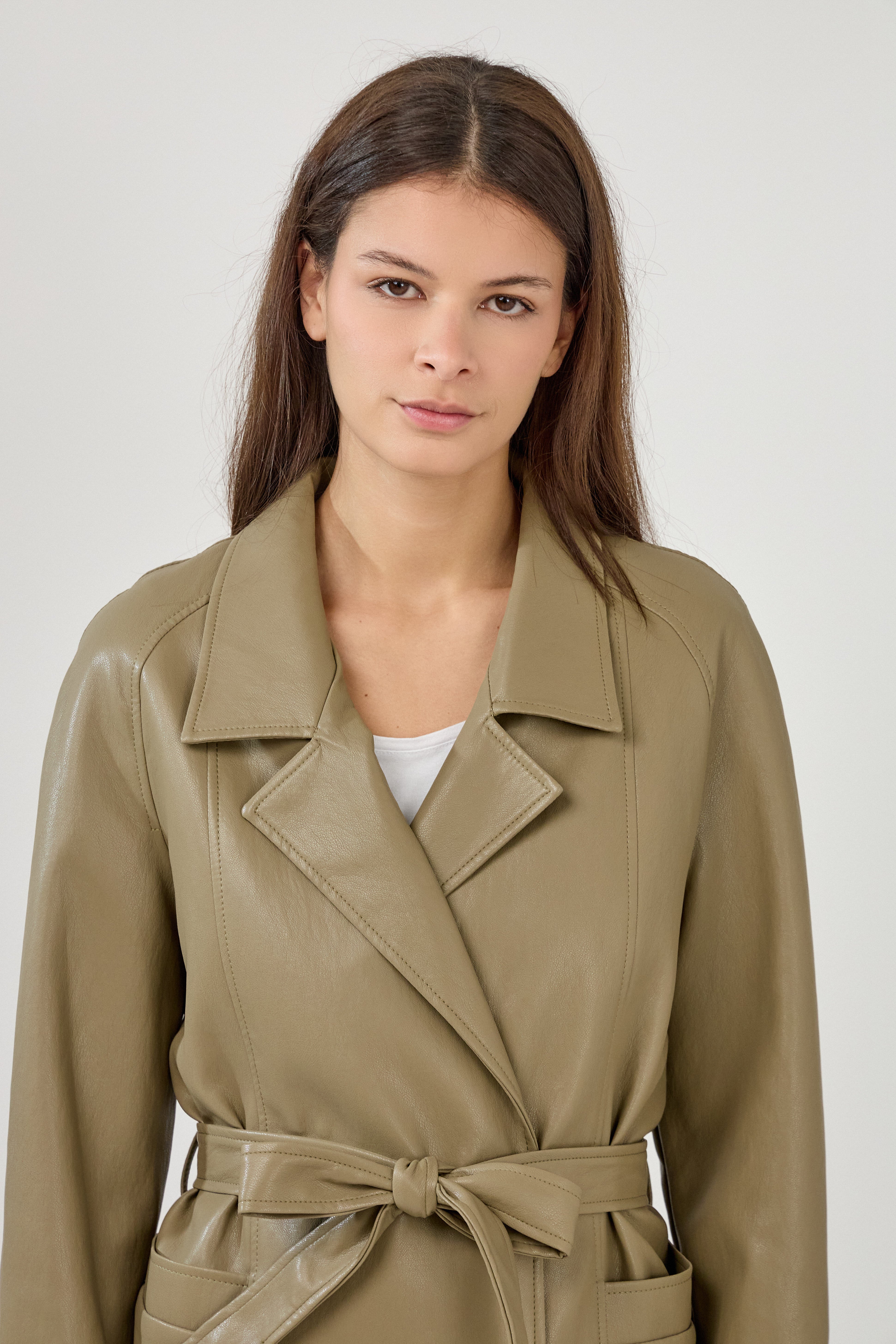 Femme portant veste ovania kaki en similicuir, veste de tailleur col à revers, découpes verticales, fermeture à boutons, ceinture et passants, zoom devant
#couleur_kaki