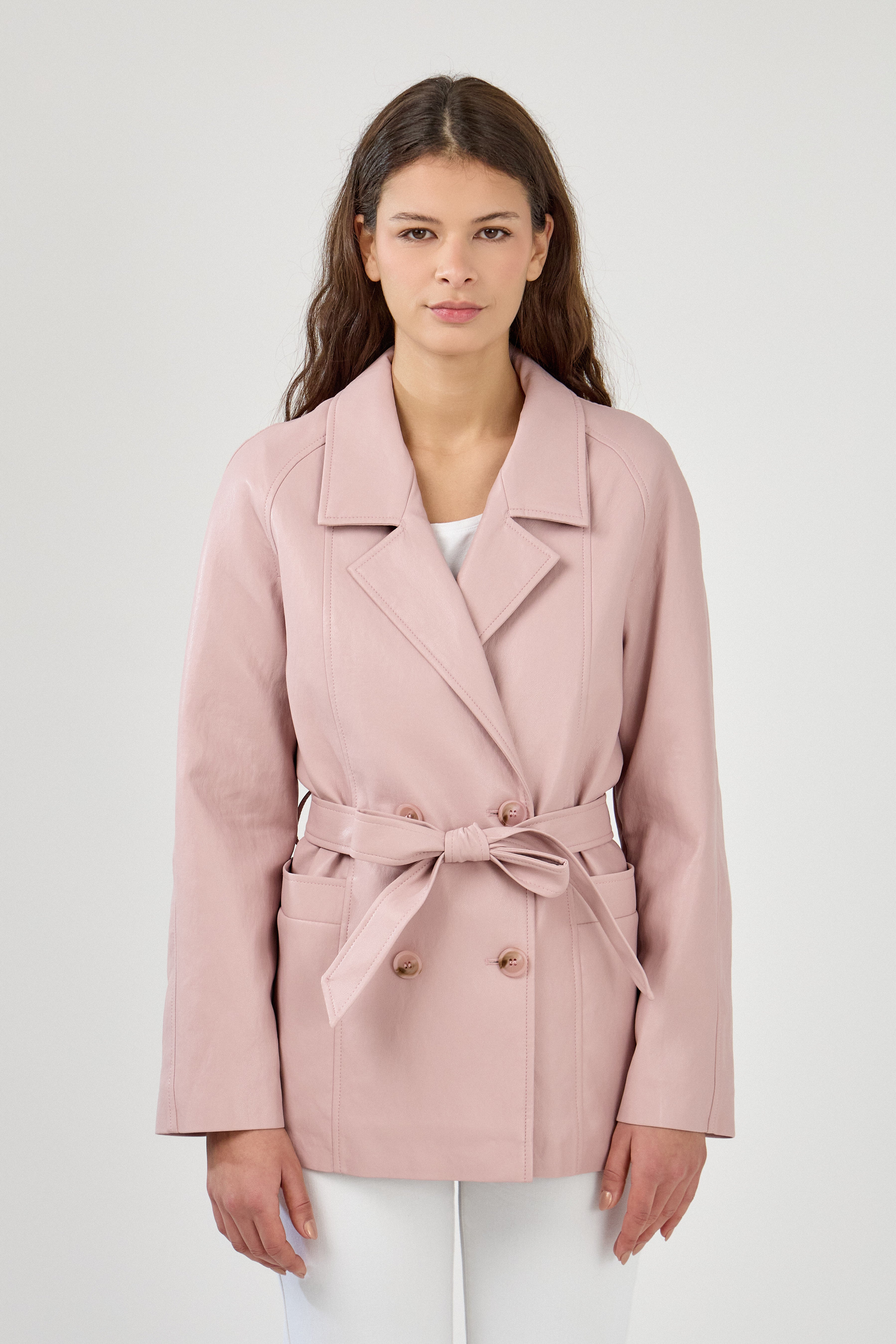 Femme portant veste ovania rose pâle en similicuir, veste de tailleur col à revers, découpes verticales, fermeture à boutons, ceinture et passants, devant
#couleur_rose