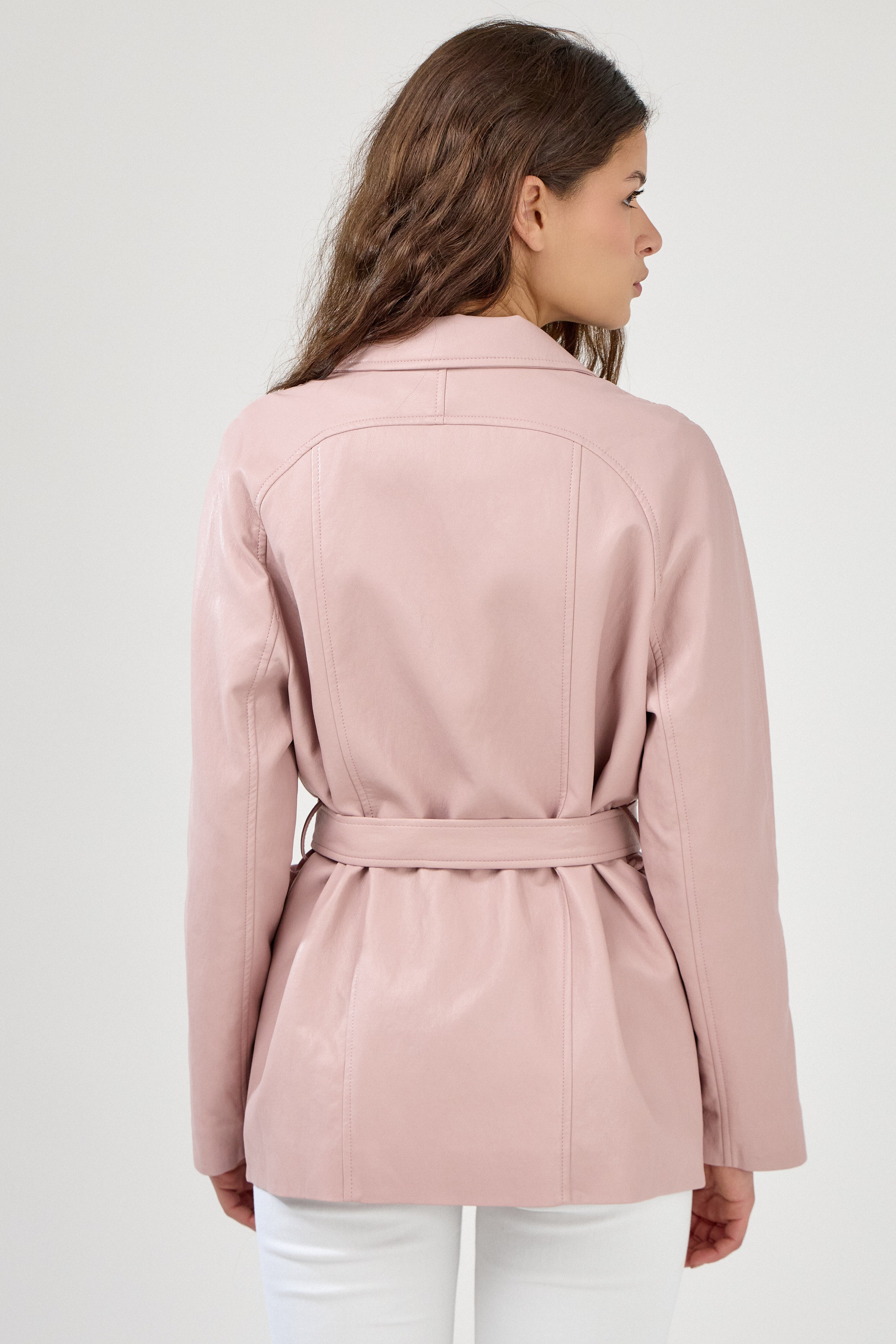 Femme portant veste ovania rose pâle en similicuir, veste de tailleur col à revers, découpes verticales, fermeture à boutons, ceinture et passants, dos
#couleur_rose