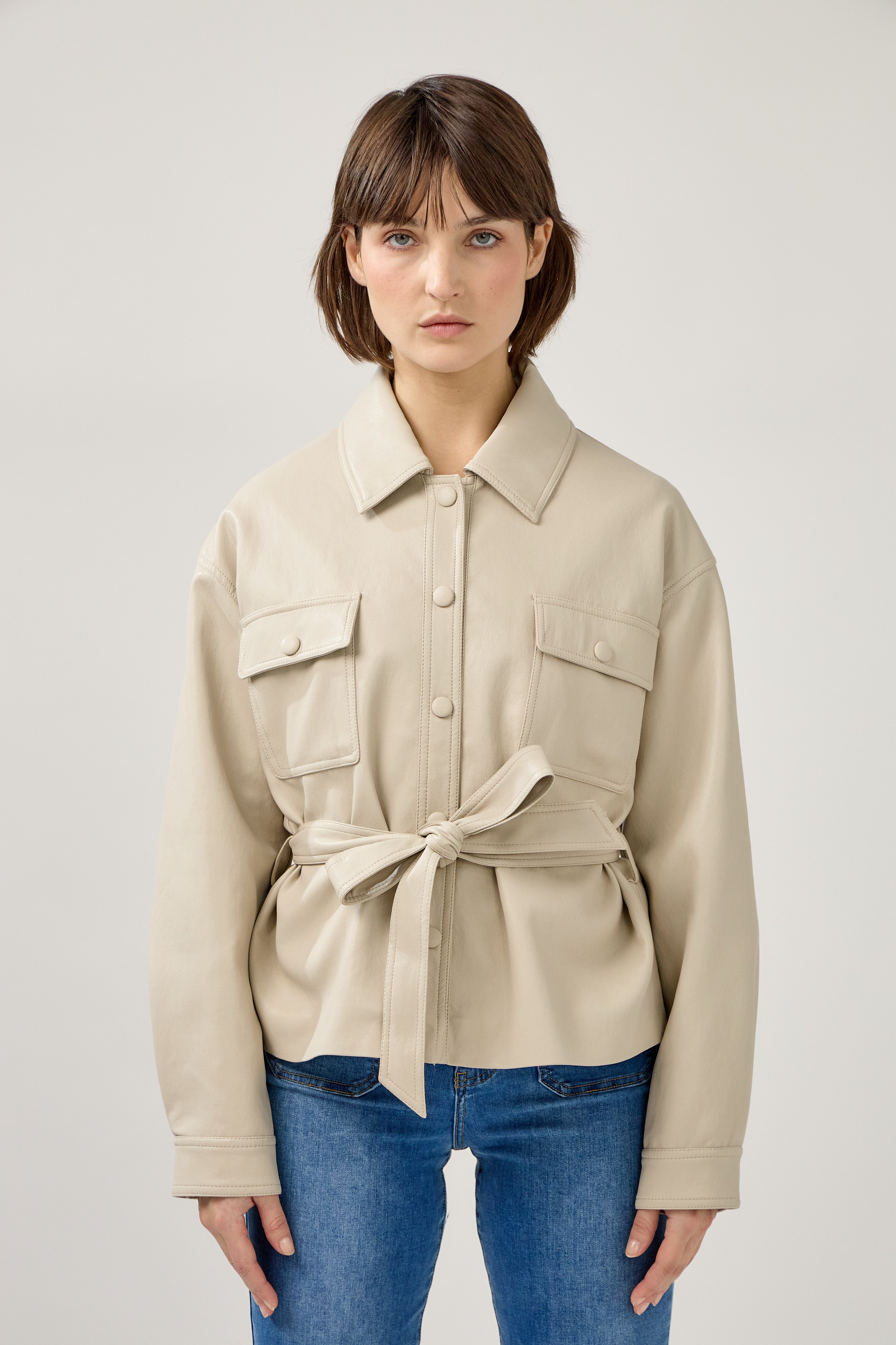 veste en similicuir à ceinture, col français, poches plaquées à rabats boutonnées poitrine, boutonnière avant boutons pressions, devant
#couleur_beige