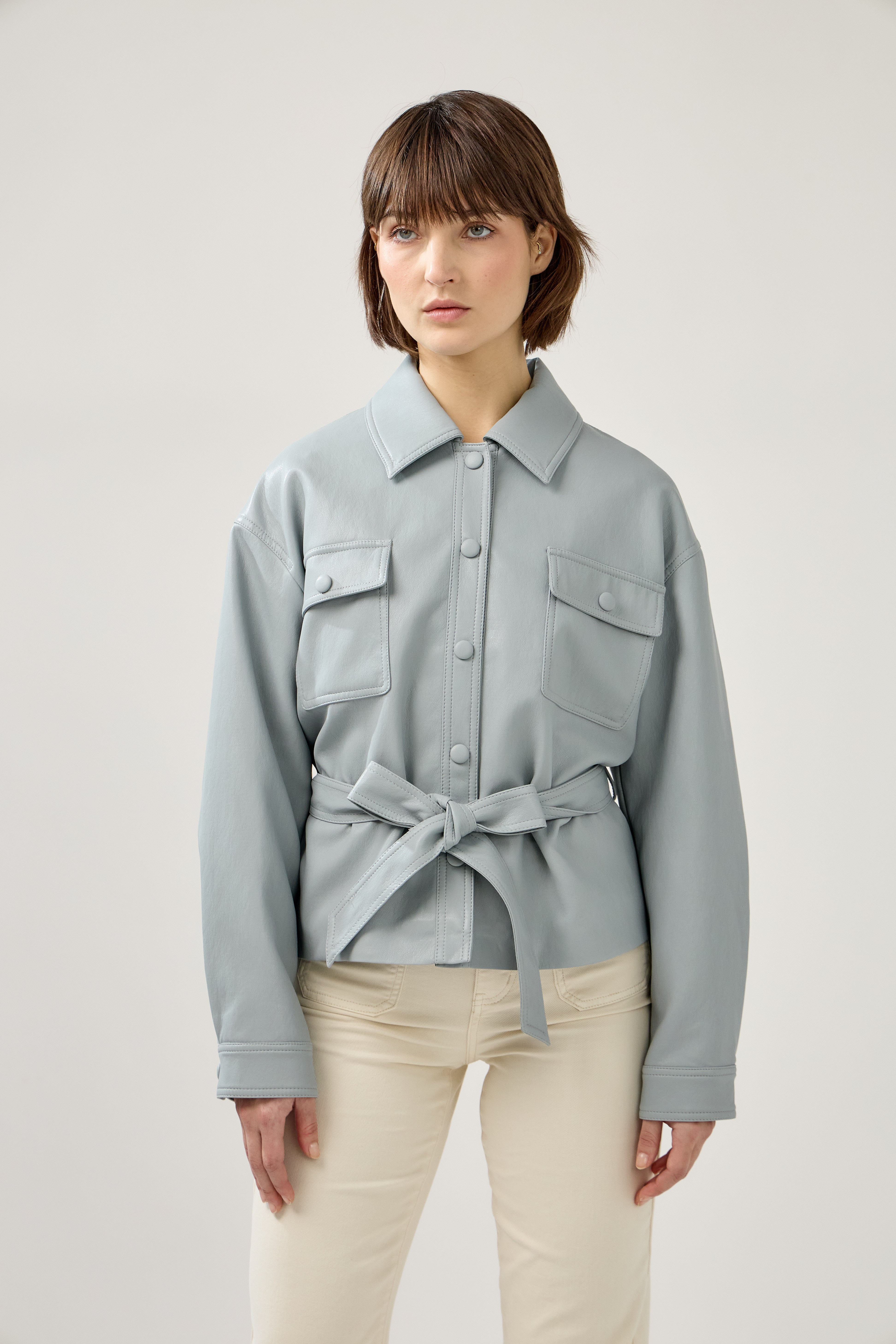 veste en similicuir à ceinture, col français, poches plaquées à rabats boutonnées poitrine, boutonnière avant boutons pressions, devant
#couleur_ciel