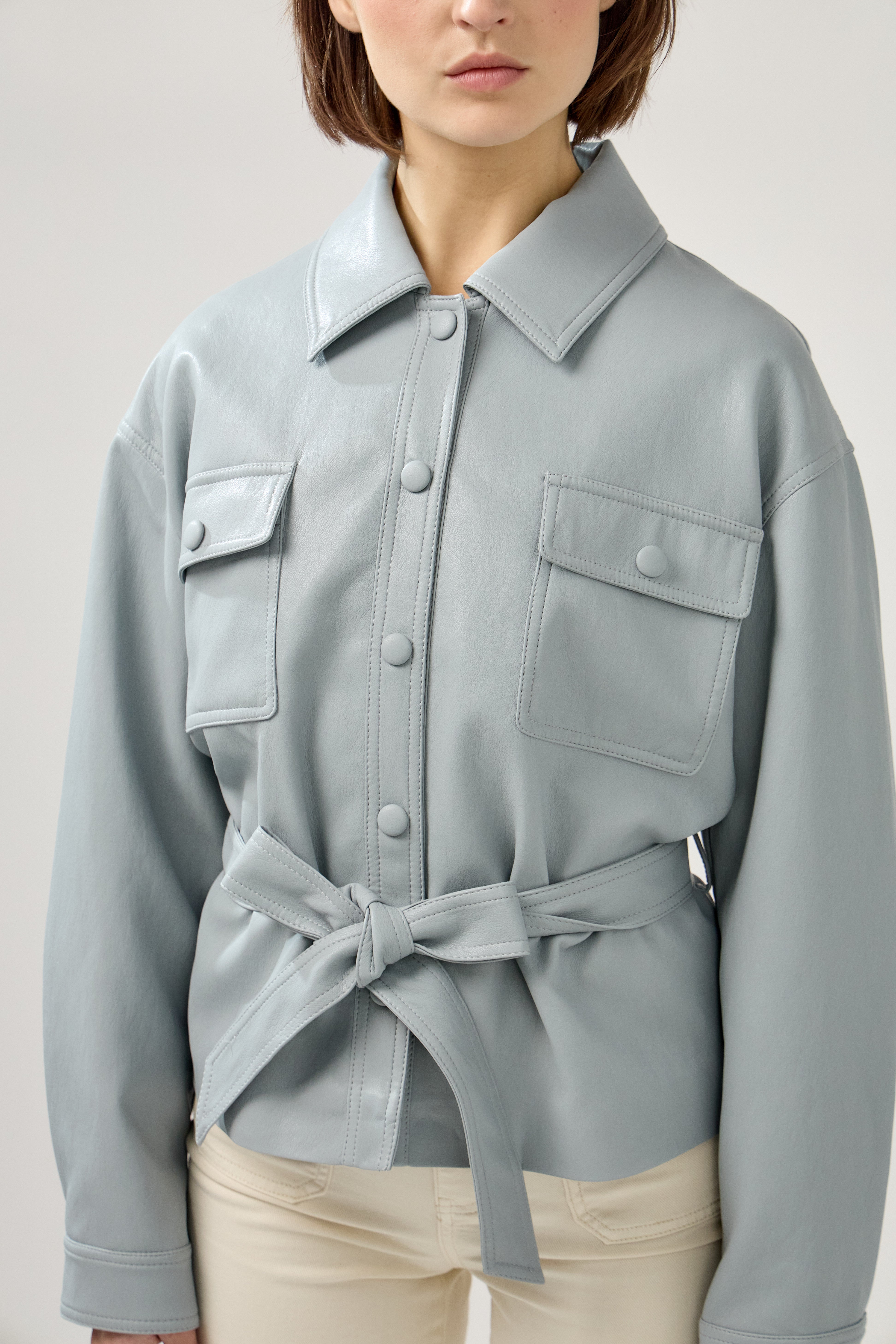 veste en similicuir à ceinture, col français, poches plaquées à rabats boutonnées poitrine, boutonnière avant boutons pressions, zoom devant
#couleur_ciel