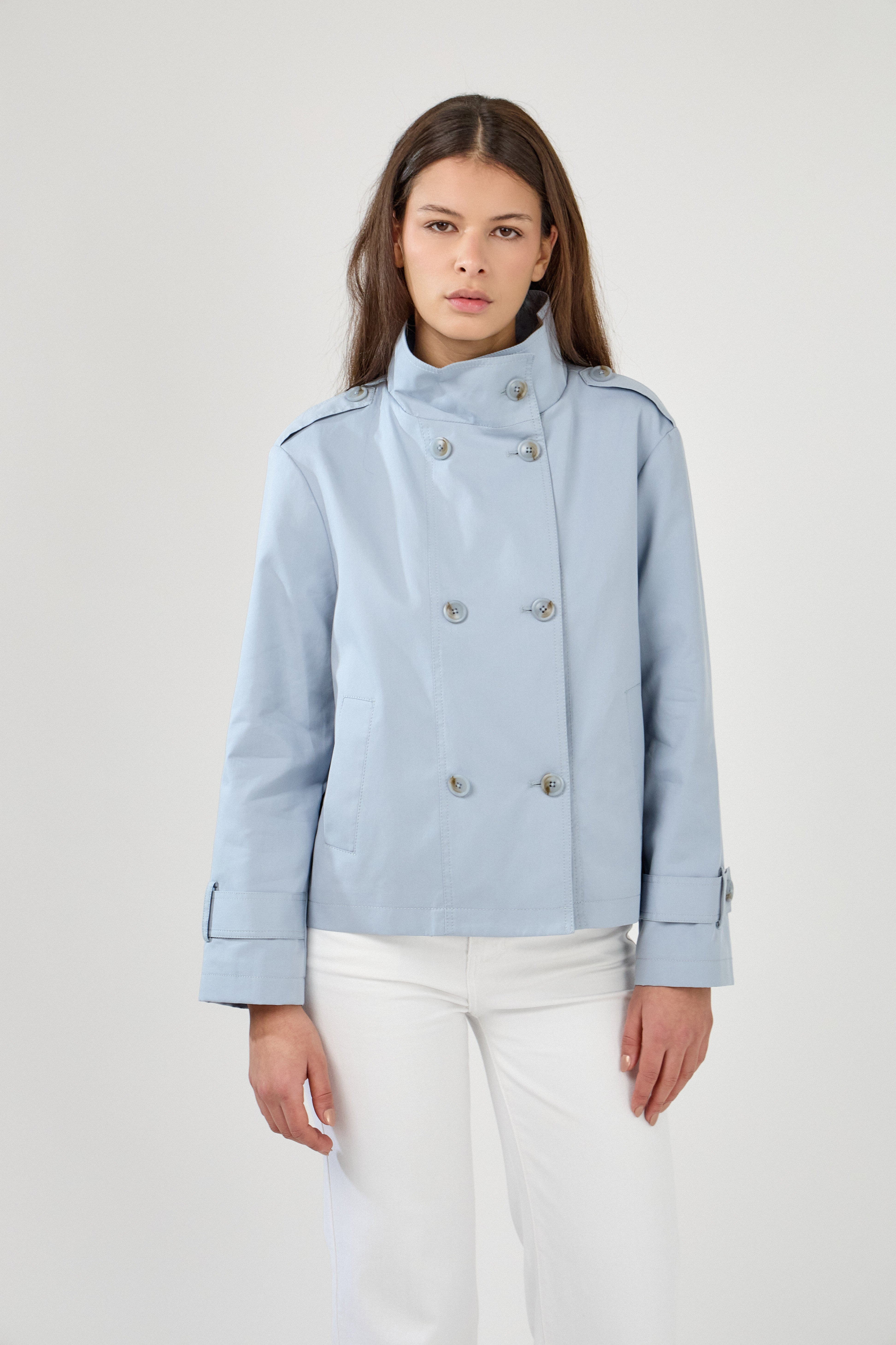 femme portant la veste trench col montant Lynara bleu ciel, tenue chic féminine, fermeture à boutons et poches raglans, pattes de serrage décorative au poignets, devant
#couleur_ciel