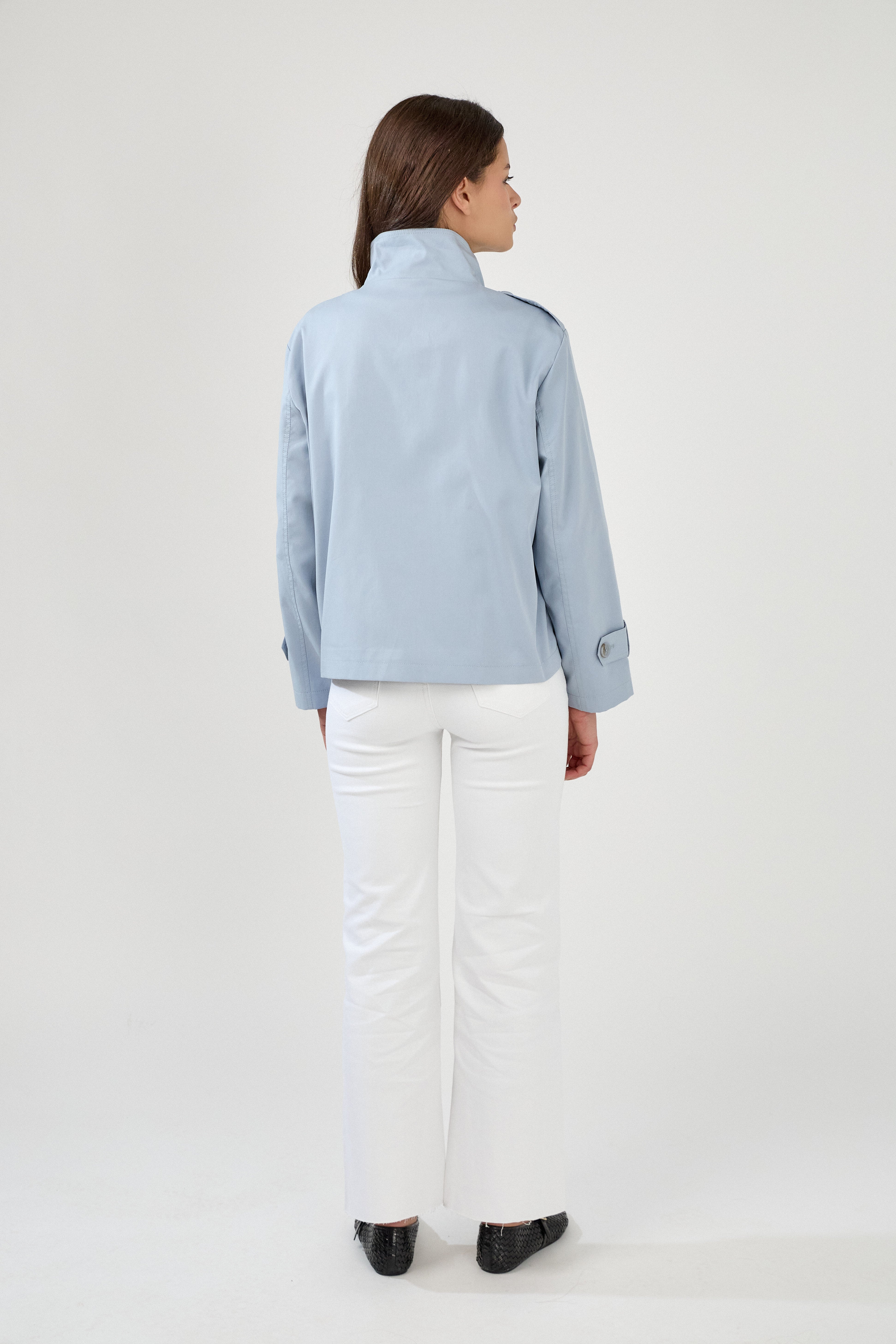 femme portant la veste trench col montant Lynara bleu ciel, tenue chic féminine, fermeture à boutons et poches raglans, pattes de serrage décorative au poignets, dos
#couleur_ciel