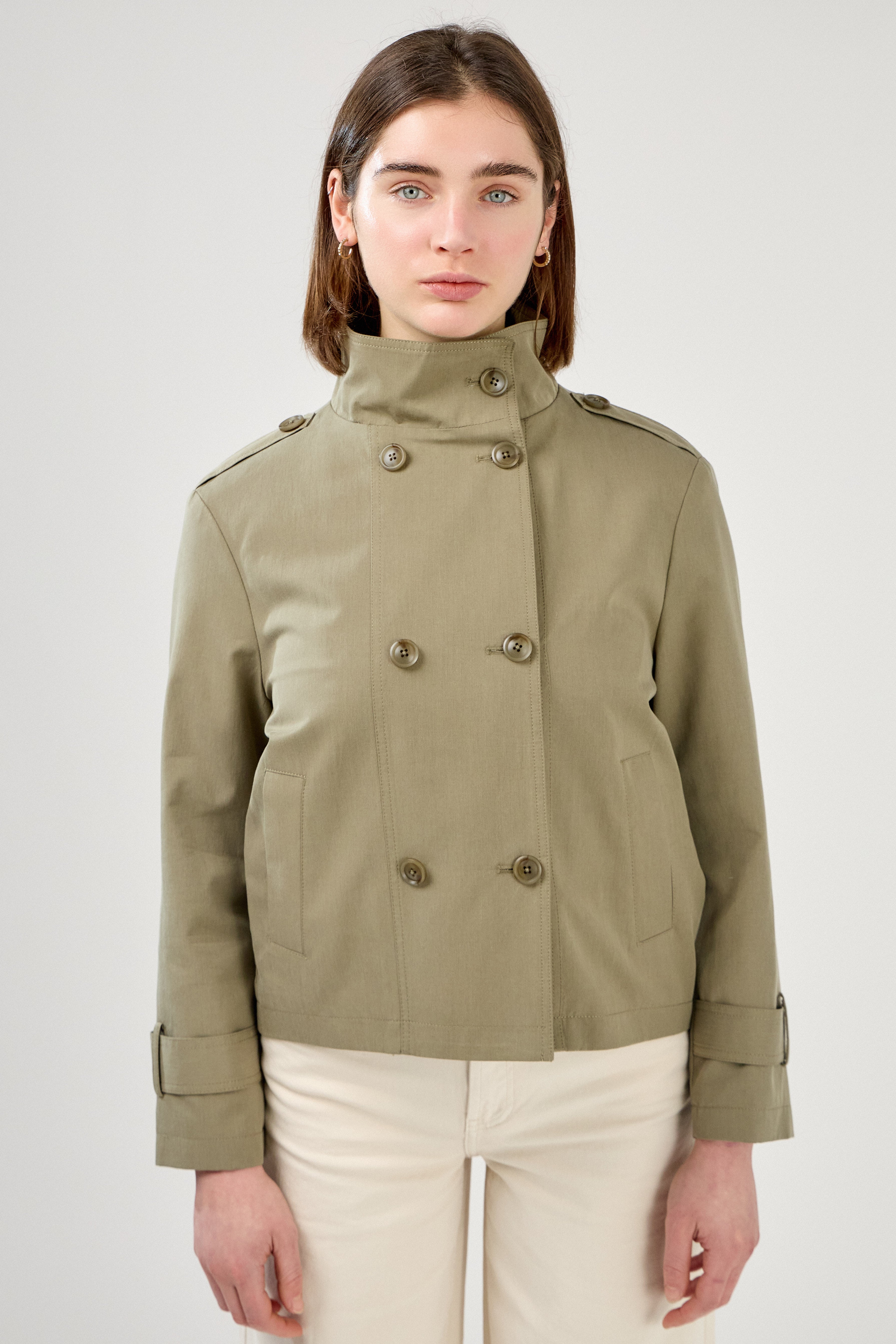 femme portant la veste trench col montant Lynara kaki clair, tenue chic féminine, fermeture à boutons et poches raglans, pattes de serrage décorative au poignets, devant
#couleur_kaki