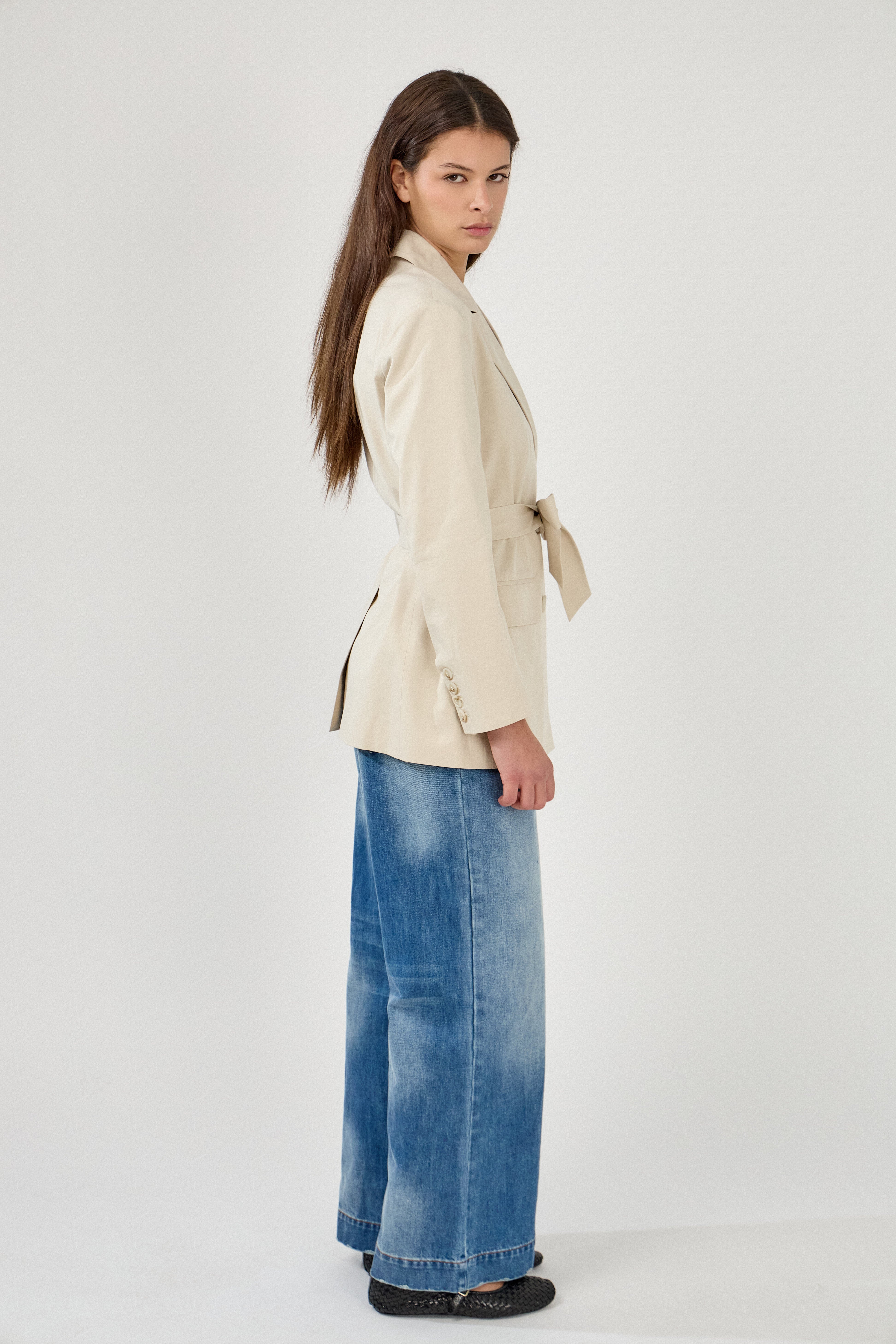 femme portant un blazer en coton beige clair, ceinture, boutons, col à revers, taille droit coupe élégante, côté
#couleur_beige