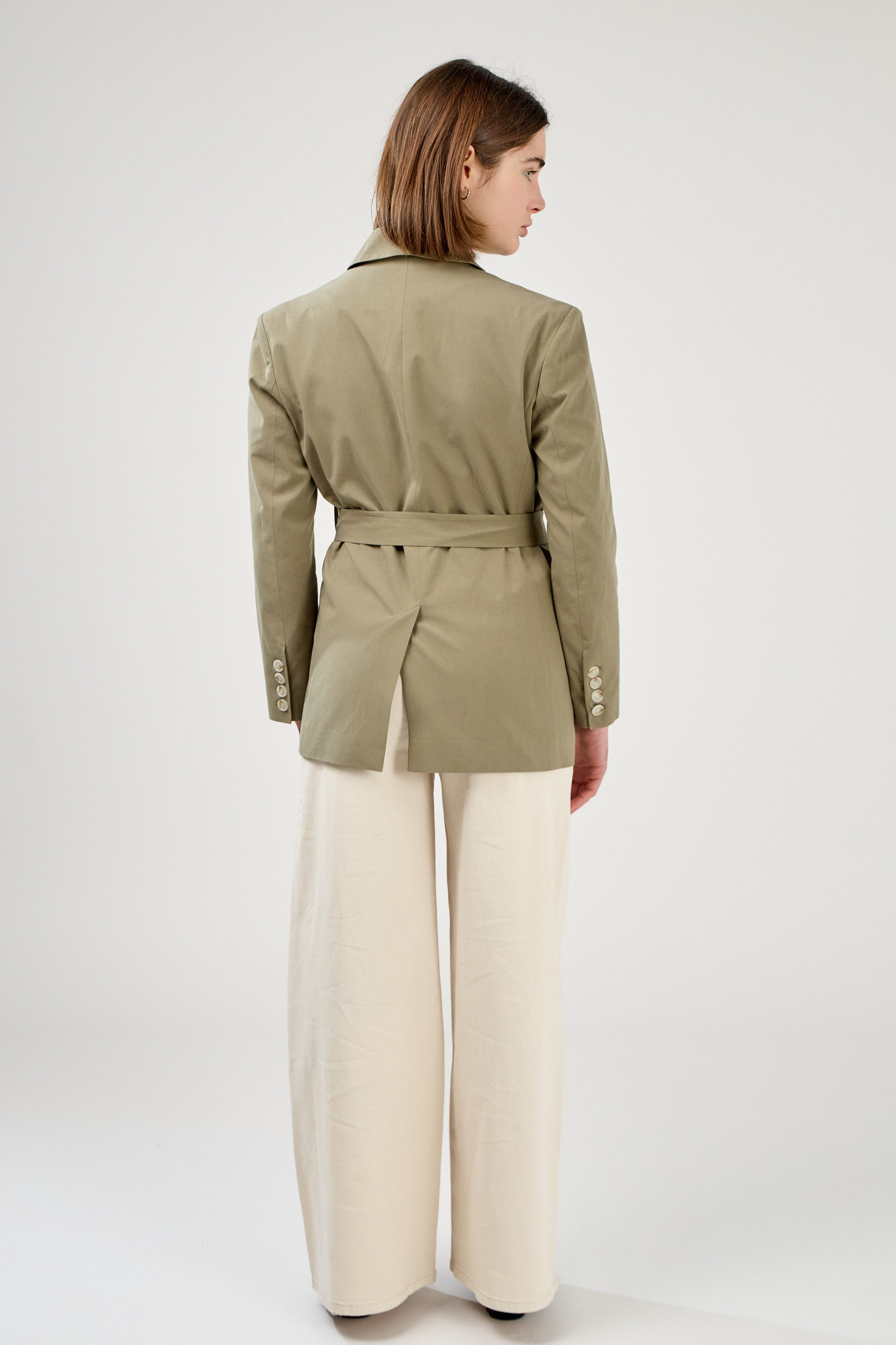 femme portant un blazer en coton kaki clair, ceinture, fente bas milieu dos et poignets à boutons, col à revers, taille droit coupe élégante, dos
#couleur_kaki