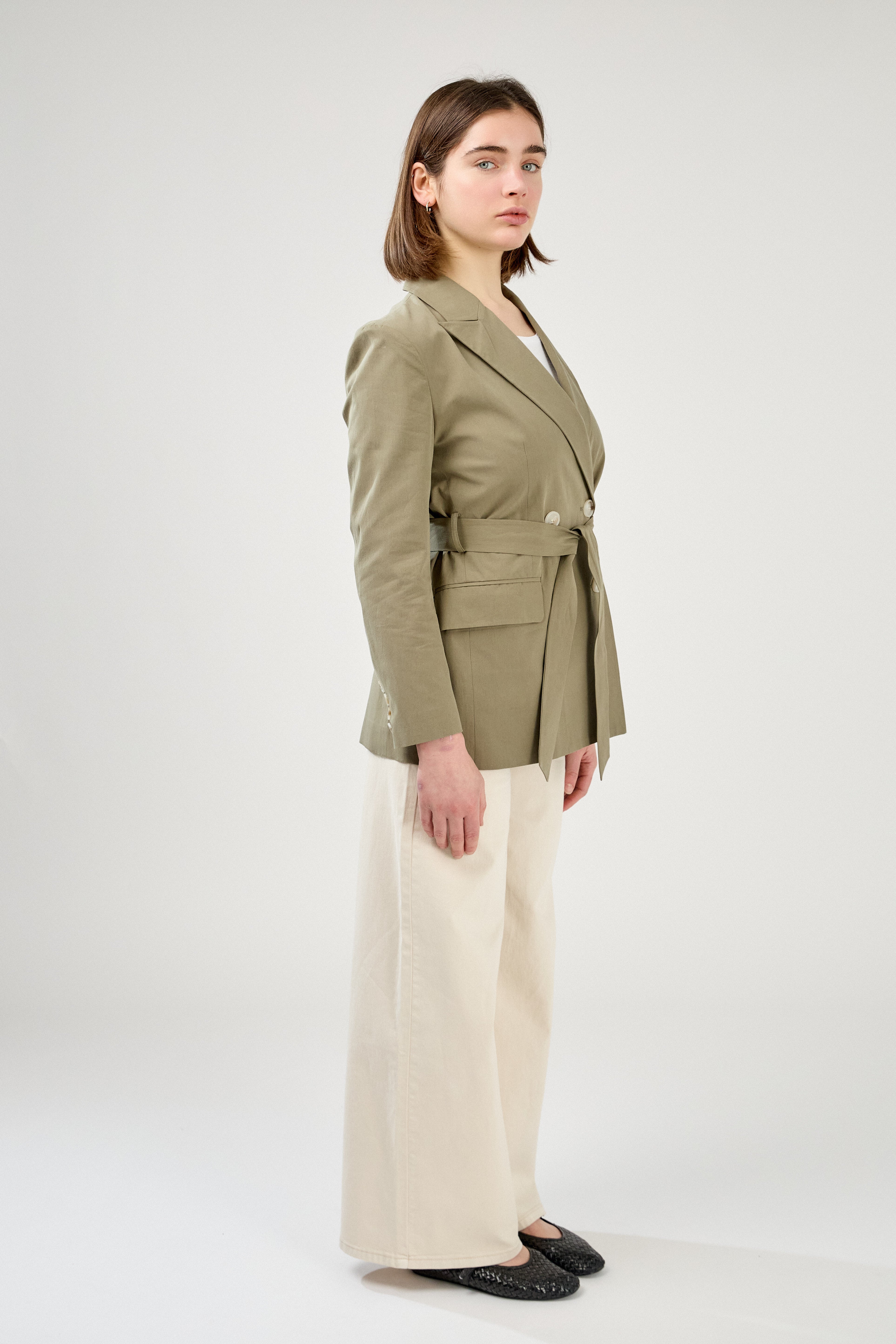 femme portant un blazer en coton kaki clair, ceinture, boutons, col à revers, taille droit coupe élégante, côté
#couleur_kaki
