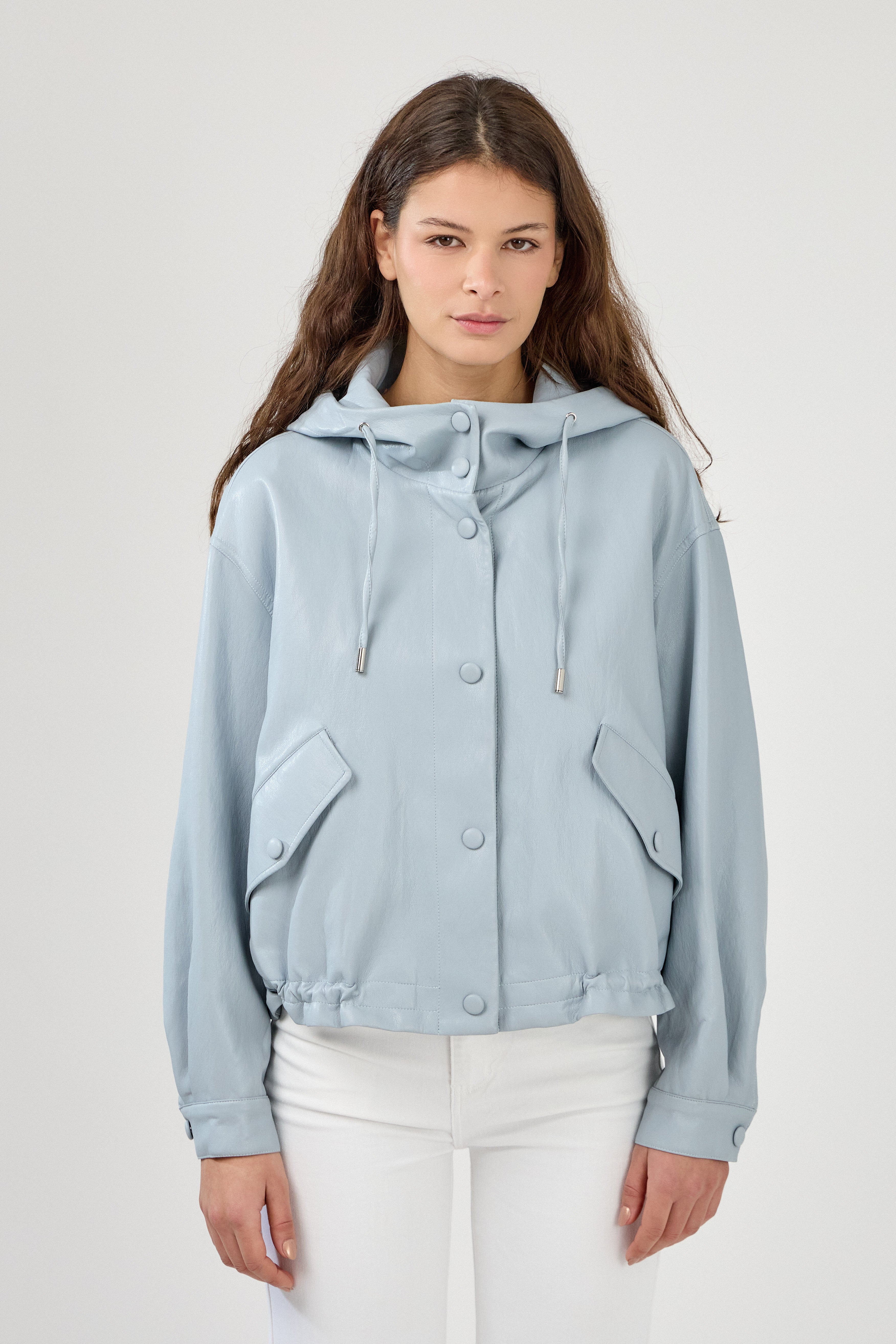 femme portant un blouson en similicuir, fermeture à boutons pression, manches larges refermées par un bouton au poignet, capuche à cordons, poches à rabats et bas ajustable avec élastique, zoom devant
#couleur_ciel