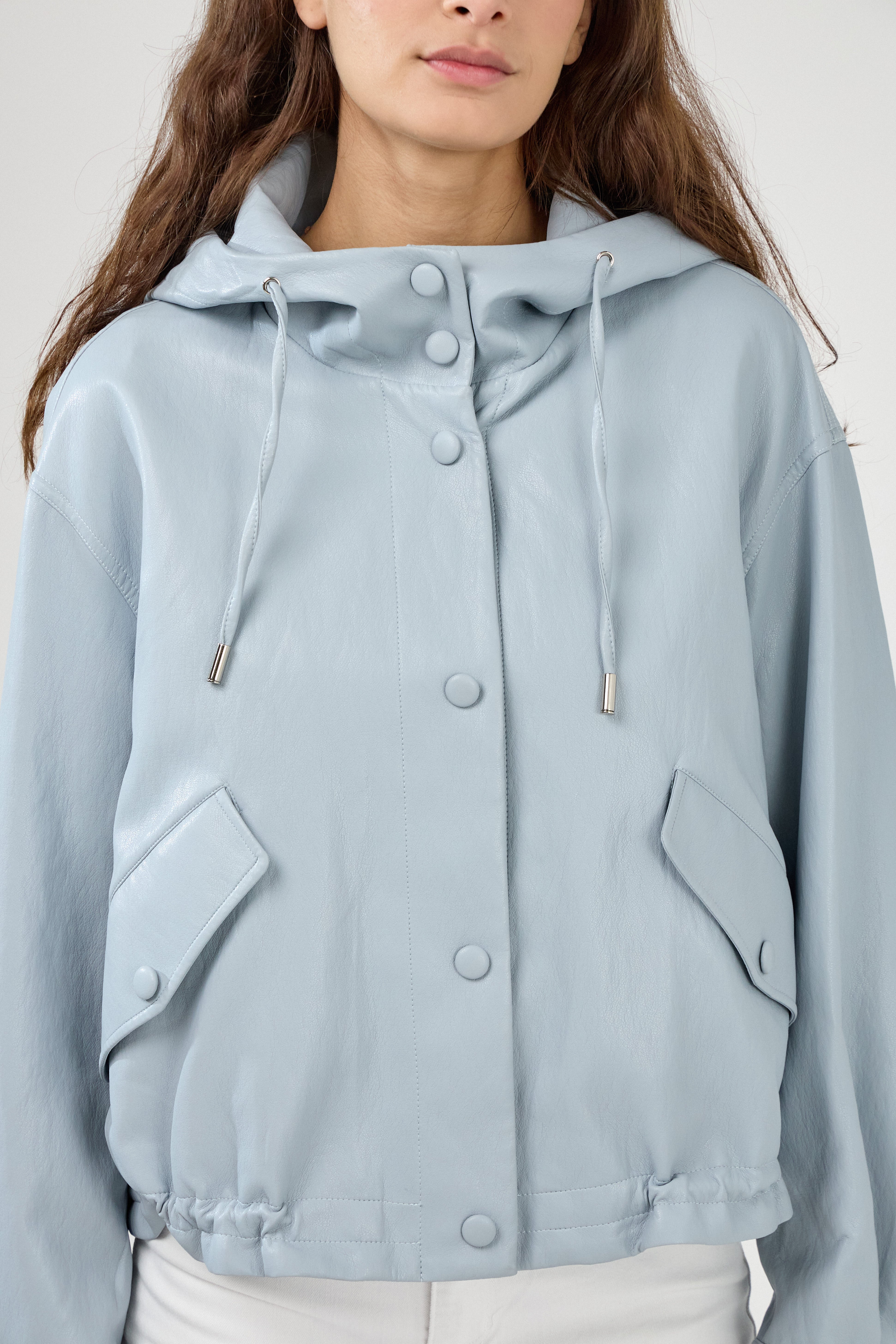 femme portant un blouson en similicuir, fermeture à boutons pression, manches larges refermées par un bouton au poignet, capuche à cordons, poches à rabats et bas ajustable avec élastique, zoom devant
#couleur_ciel