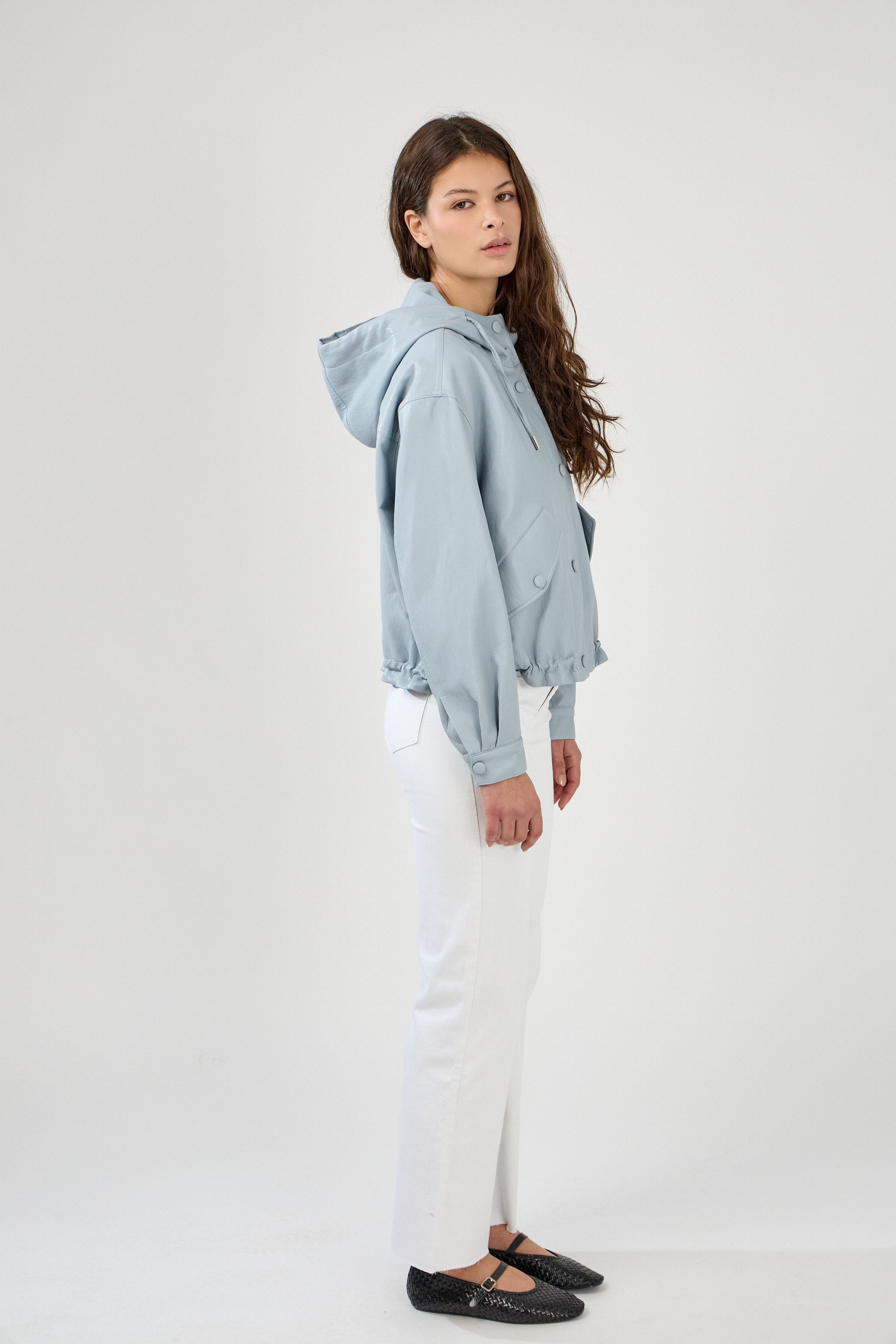 femme portant un blouson en similicuir, fermeture à boutons pression, manches larges refermées par un bouton au poignet, capuche à cordons, poches à rabats et bas ajustable avec élastique, côté
#couleur_ciel