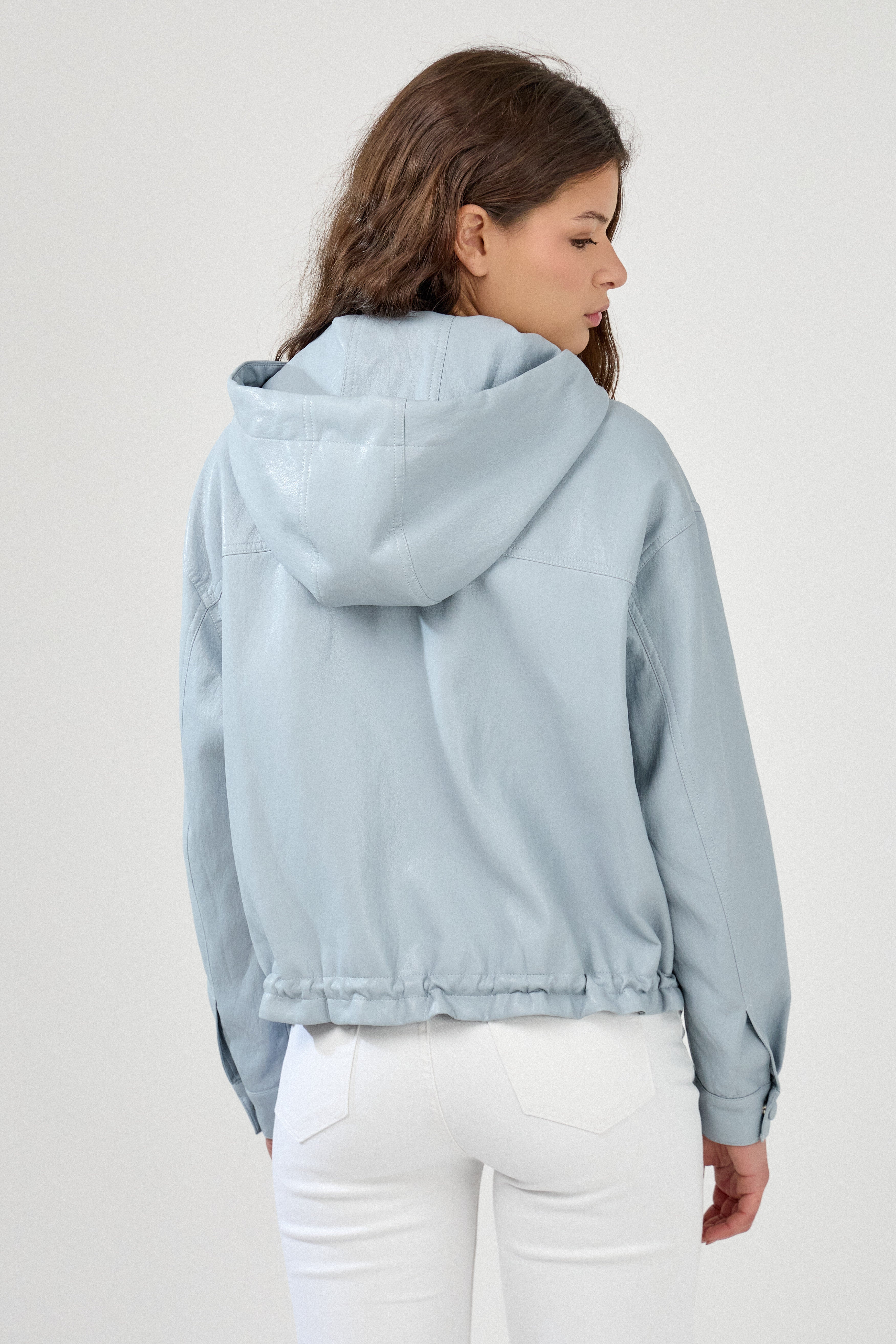 femme portant un blouson en similicuir, fermeture à boutons pression, manches larges refermées par un bouton au poignet, capuche à cordons, poches à rabats et bas ajustable avec élastique, dos
#couleur_ciel