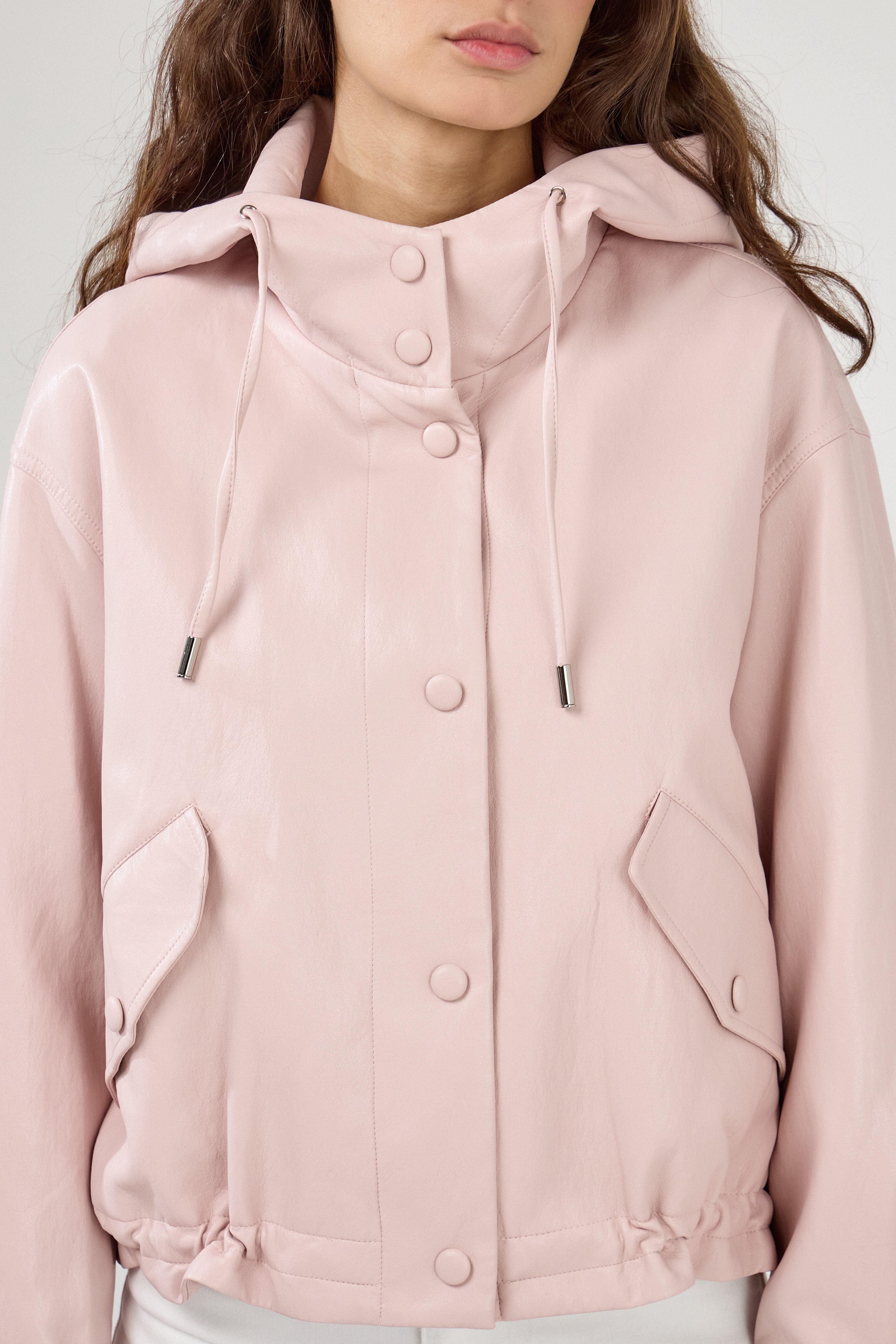 femme portant un blouson en similicuir, fermeture à boutons pression, manches larges refermées par un bouton au poignet, capuche à cordons, poches à rabats et bas ajustable avec élastique, zoom devant
#couleur_rose