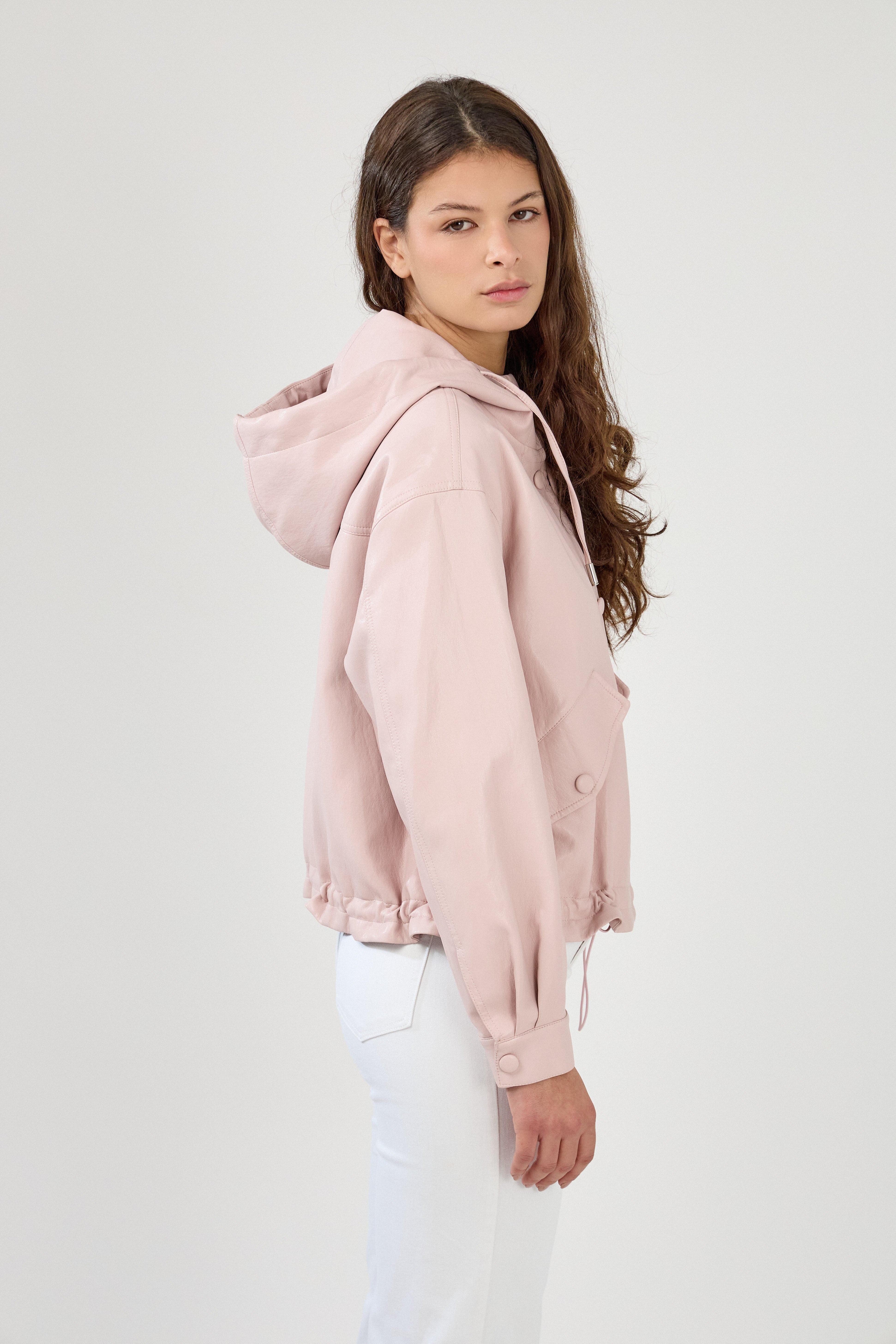 femme portant un blouson en similicuir, fermeture à boutons pression, manches larges refermées par un bouton au poignet, capuche à cordons, poches à rabats et bas ajustable avec élastique, côté
#couleur_rose