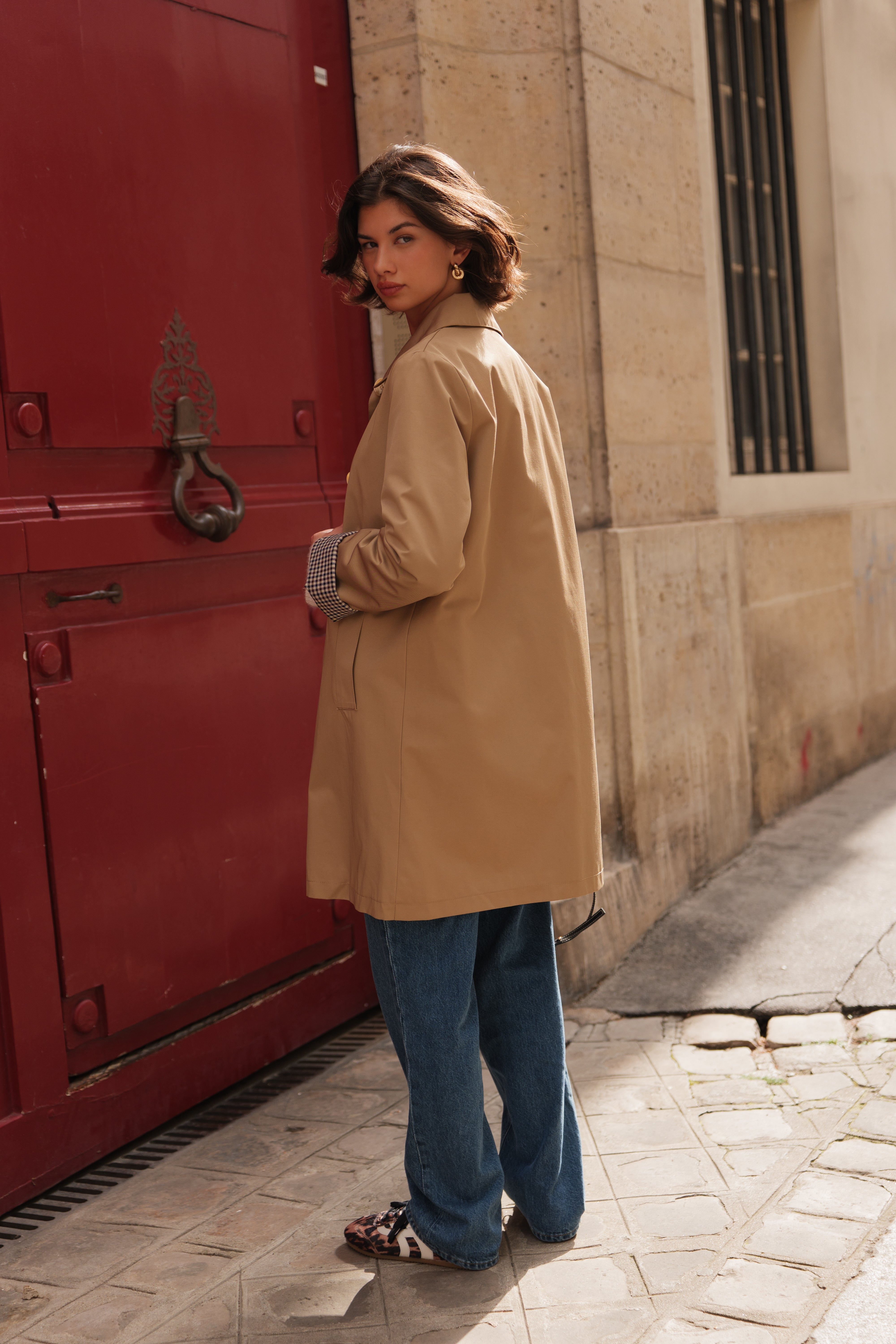Femme portant le trench LESLEY Escandelle en matière déperlante beige – vue de face – look chic parisien avec revers à petits carreaux
#couleur_beige